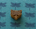 Hand-carved wooden dragonfly printing block surrounded by repeated dragonfly impressions on a textured blue surface