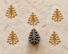 Hand carved wooden Christmas tree printing block with curved branches shown beside repeated tree impressions on handmade paper.