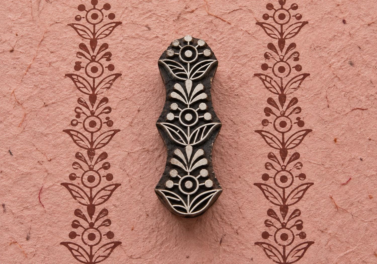Hand carved wooden Floral Totem printing block with a repeating floral border printed on textured pink handmade paper.