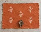 Hand carved Indian wooden printing block with a tulip motif beside repeated white tulip impressions on textured orange handmade paper