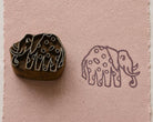 Hand carved spotted elephant wooden printing block beside its printed elephant design on textured pink handmade paper