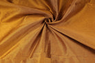 Rich golden brown polyester shantung fabric gathered to show the drape and fine textured weave.
