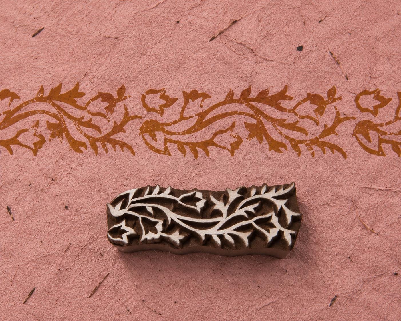 Meandering Vine Border hand carved wooden printing block with a flowing floral vine impression on handmade pink paper.