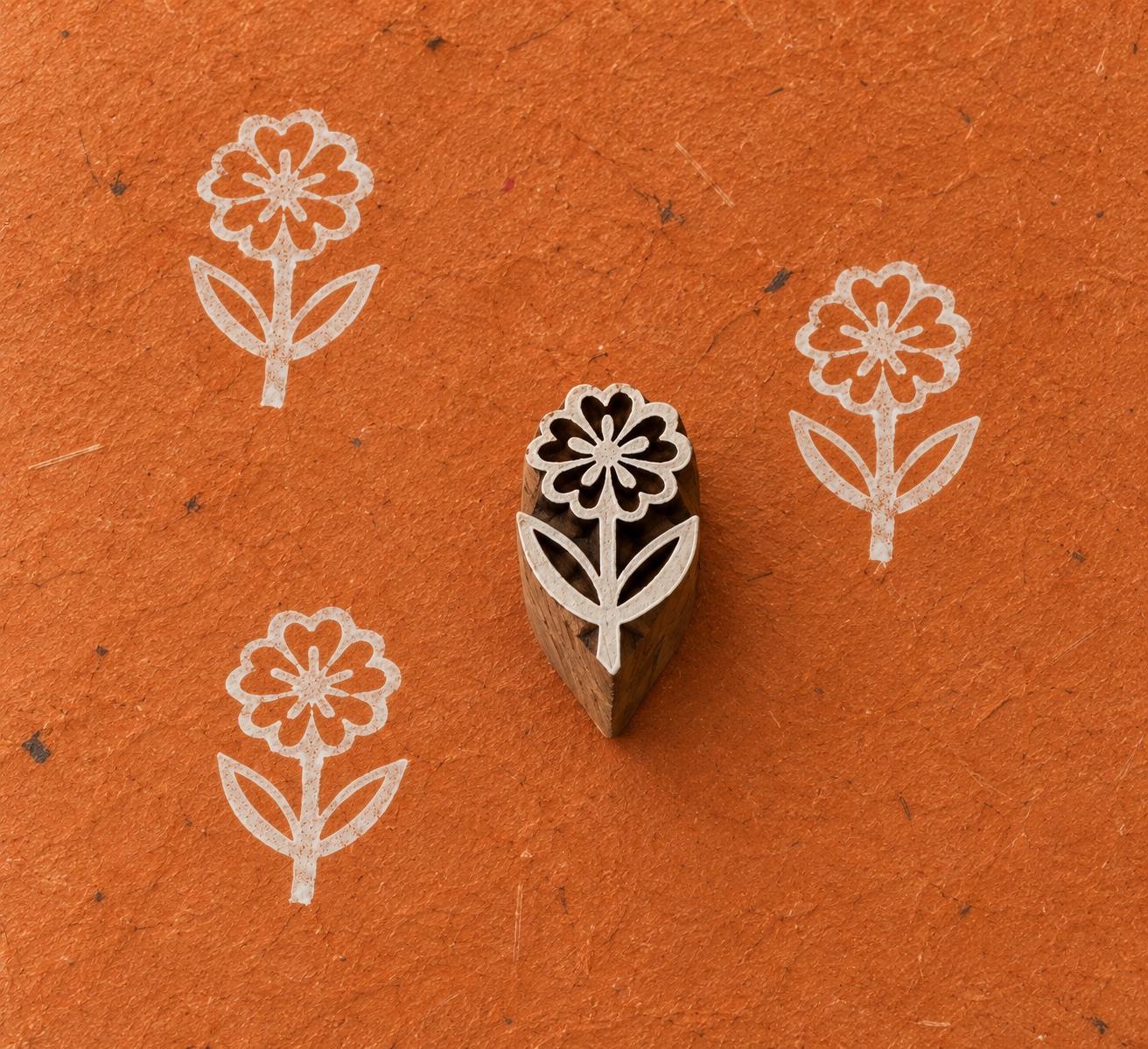 Small hand-carved Daisy Flower wooden printing block with white flower prints on textured burnt orange handmade paper.