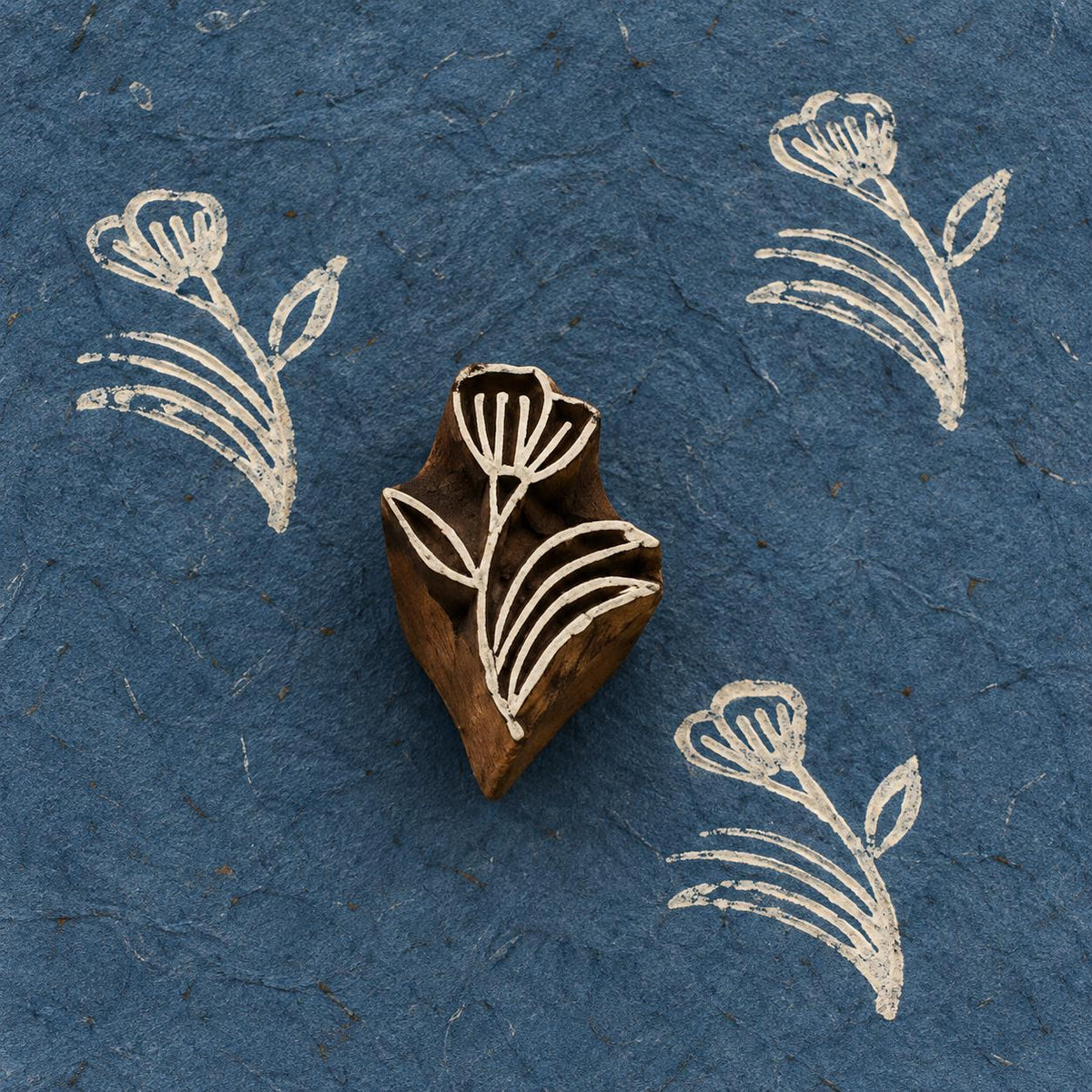 Hand-carved Meadow Bloom wooden printing block with white floral prints on textured dark blue handmade paper.