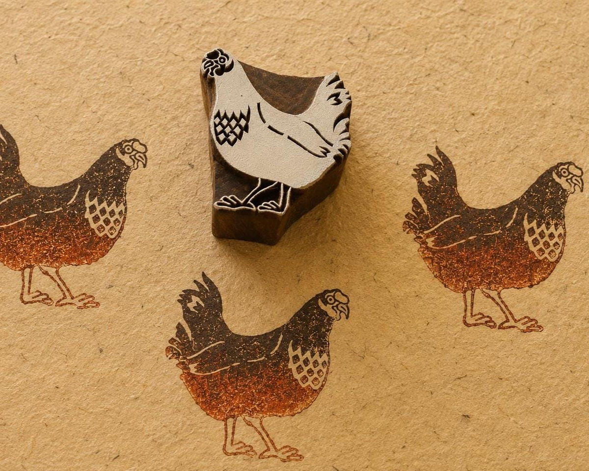 Hand-carved wooden rooster printing block surrounded by three repeated brown rooster prints on textured handmade paper.