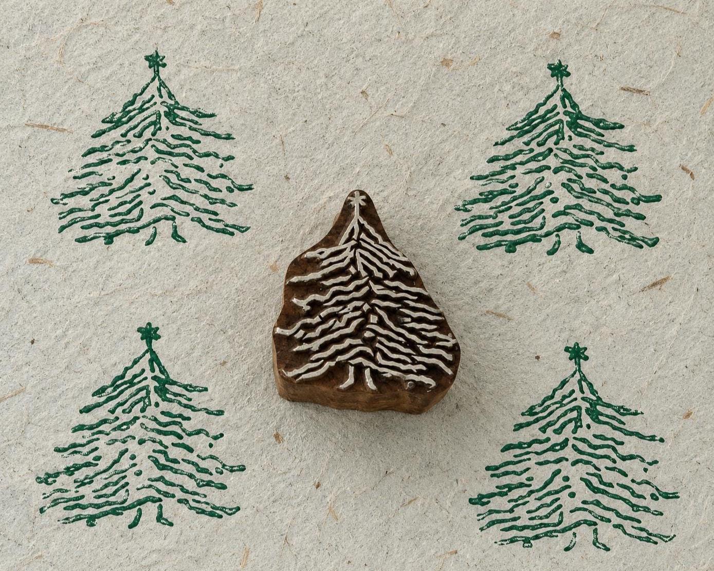 Hand carved wooden Christmas tree printing block with four green printed impressions on handmade textured paper.