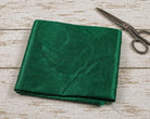 Emerald green faux silk dupioni fabric folded on a distressed white wooden table beside vintage metal scissors.