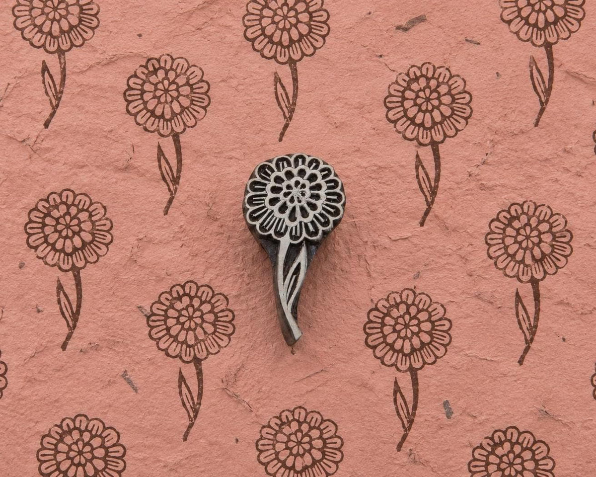 Layered Bloom hand carved wooden printing block with repeated round floral impressions on textured handmade pink paper.
