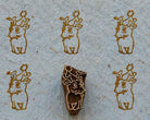 Hand carved wooden baby reindeer printing block surrounded by five brown reindeer prints on textured grey handmade paper.