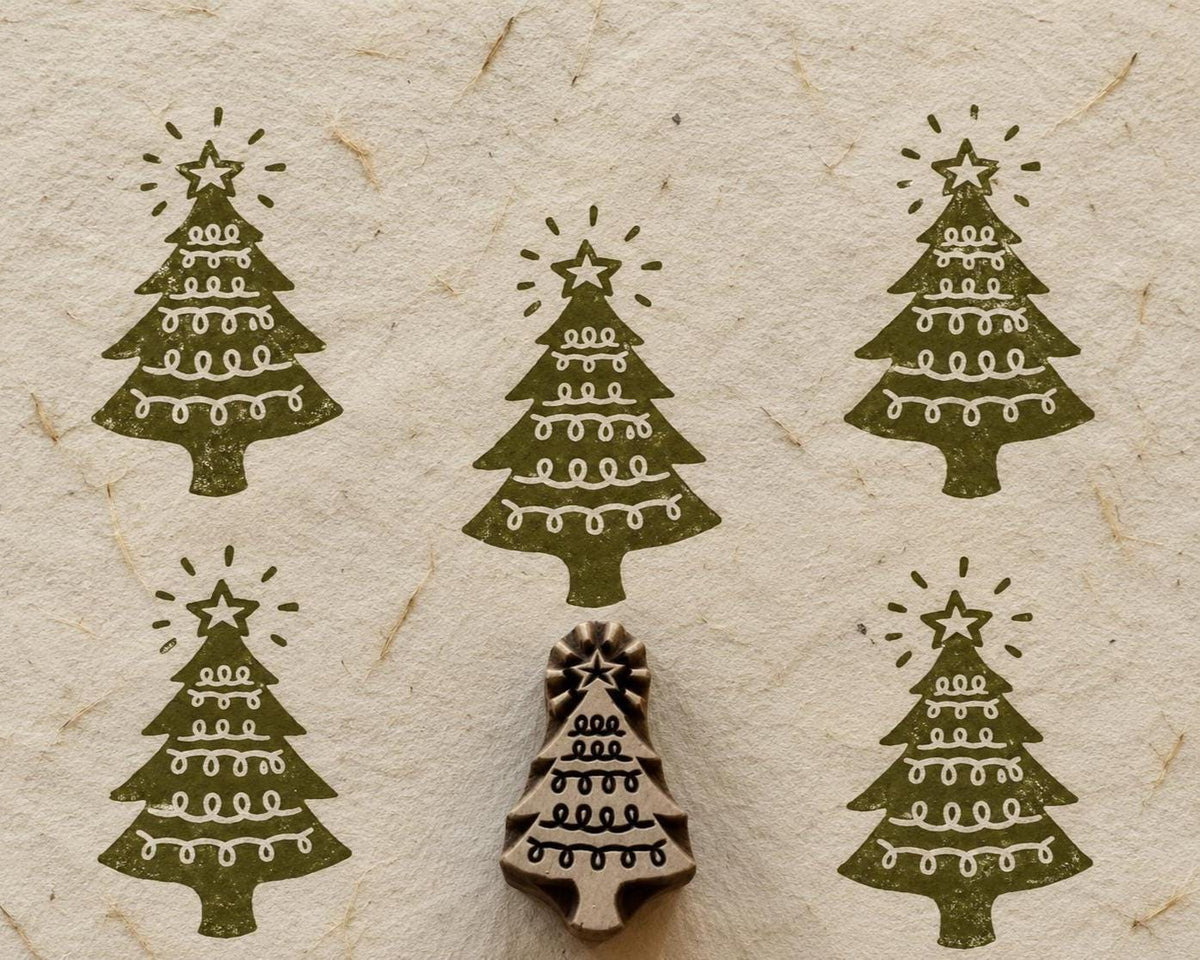 Hand carved wooden Christmas tree printing block with star and looping garland design surrounded by green prints on handmade paper