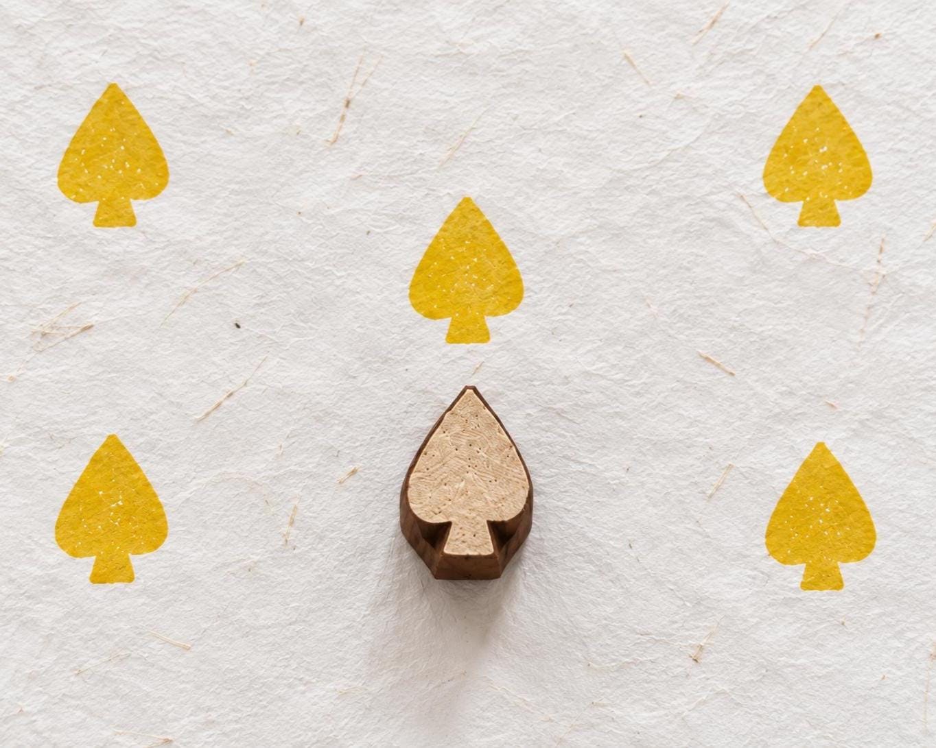 Hand carved playing card spade wooden printing block surrounded by yellow spade prints on handmade white paper