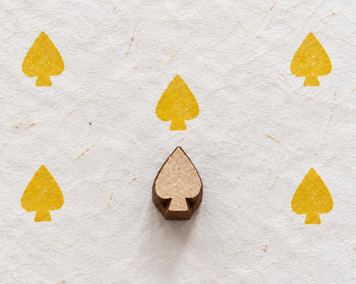 Hand carved playing card spade wooden printing block surrounded by yellow spade prints on handmade white paper
