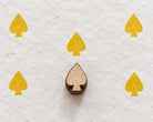 Hand carved playing card spade wooden printing block surrounded by yellow spade prints on handmade white paper