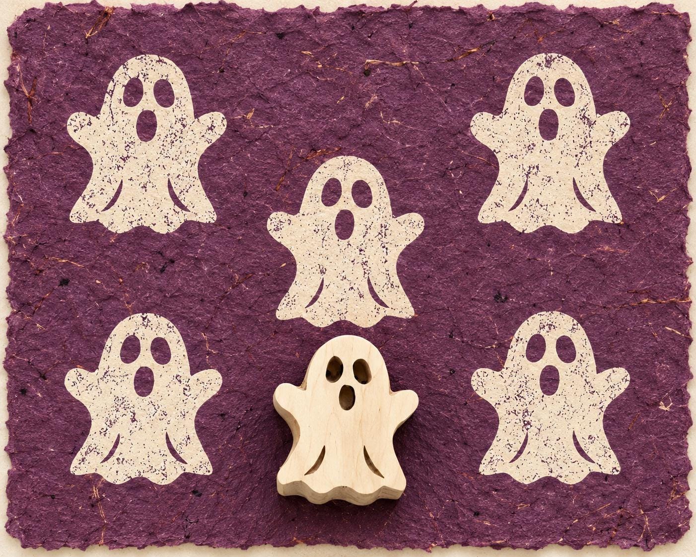 Hand carved Haunting Ghost wooden printing block with five ghost impressions on purple handmade paper.