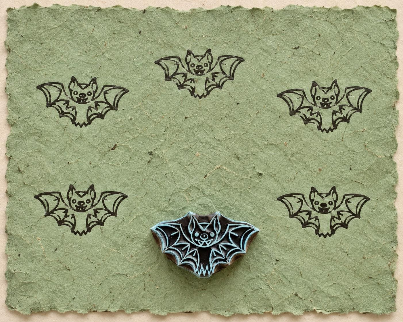 Hand carved Midnight Bat wooden printing block with five bat impressions on handmade green paper.