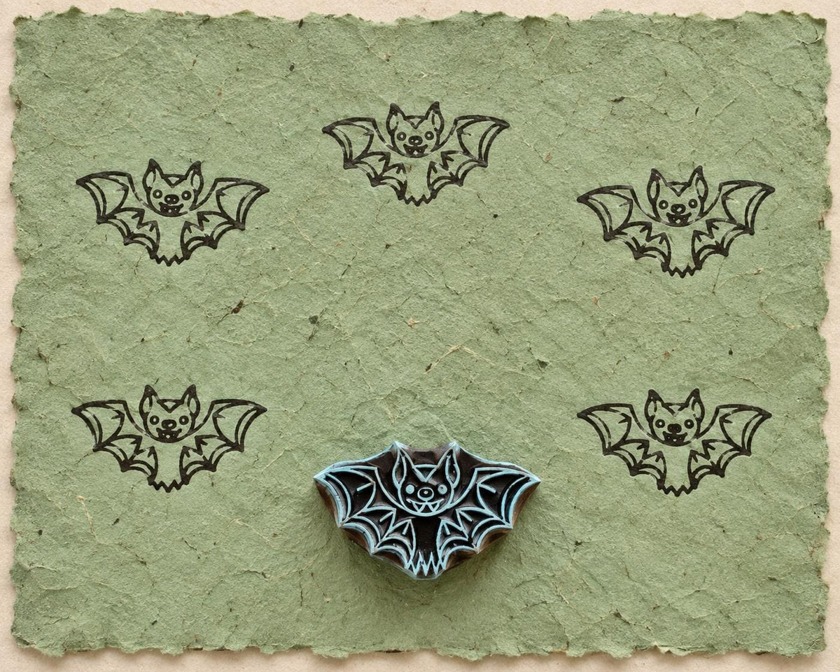 Hand carved Midnight Bat wooden printing block with five bat impressions on handmade green paper.