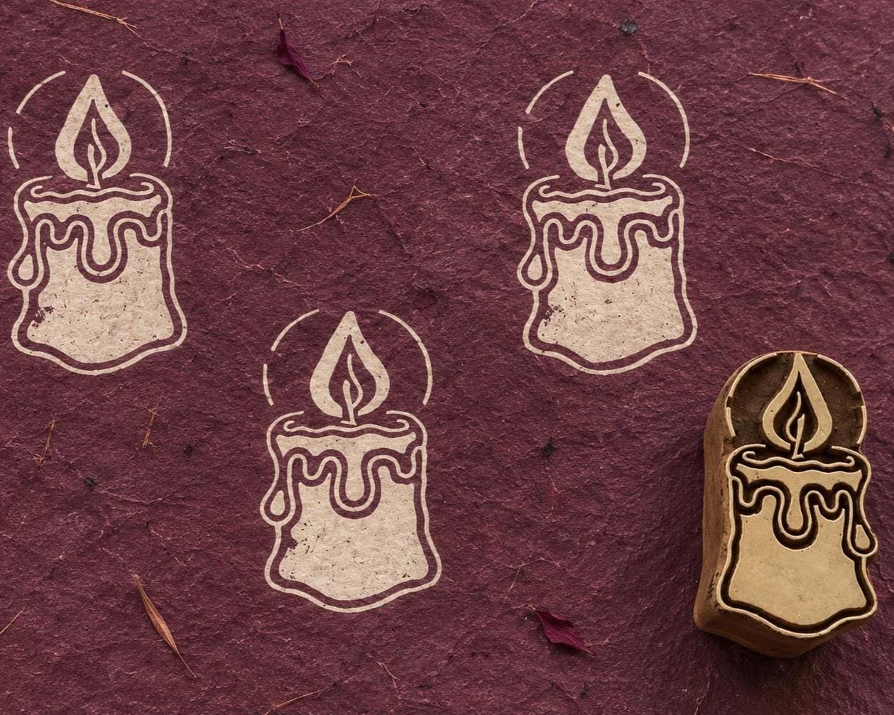 Hand carved Christmas candle wooden printing block with three cream candle impressions on a textured burgundy background