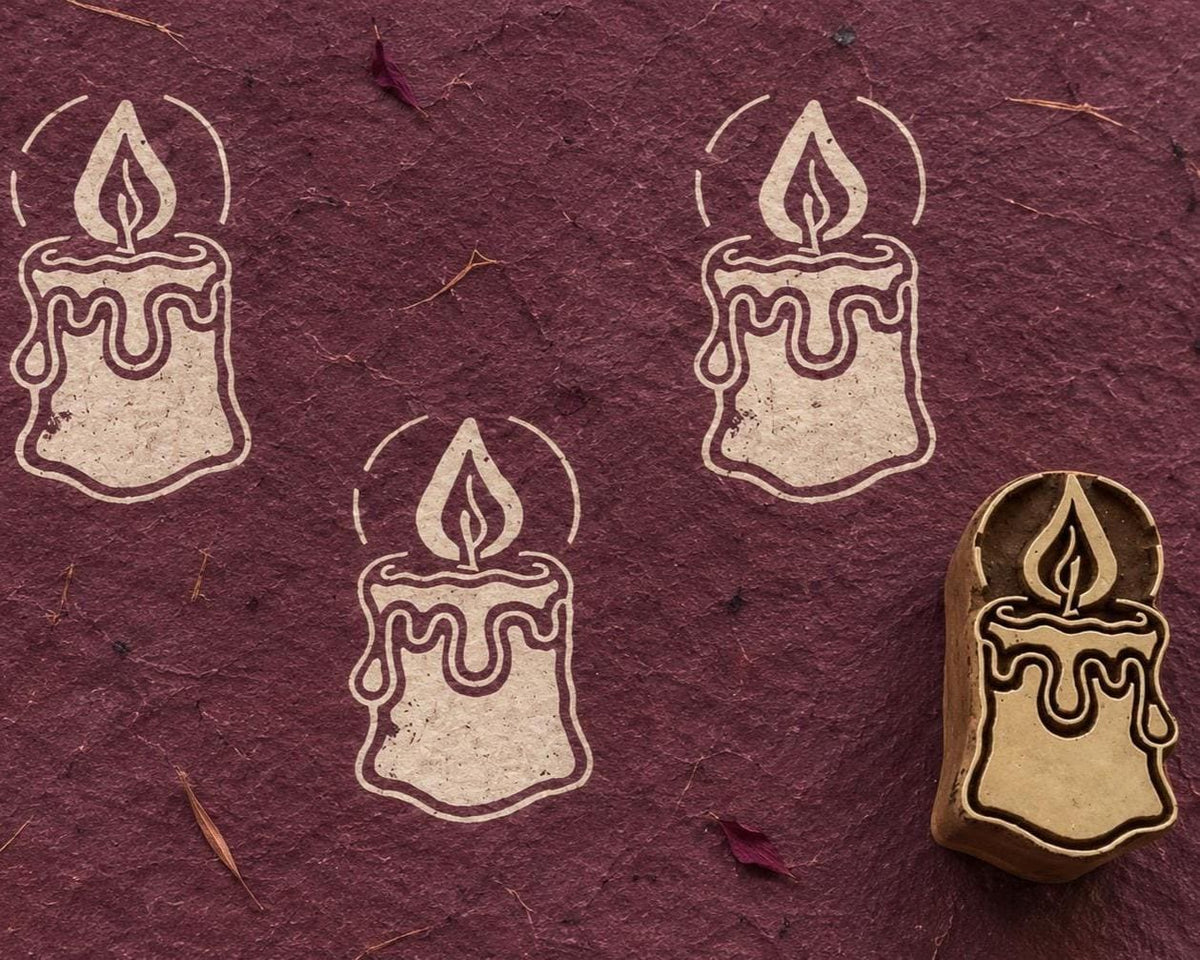 Hand carved Christmas candle wooden printing block with three cream candle impressions on a textured burgundy background