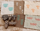 Five hand-carved wooden floral printing blocks with flower and border designs shown with colorful handmade paper prints
