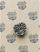 Hand carved wooden dandelion-inspired motif shown with repeated blue impressions on textured handmade paper.