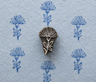 Hand carved wooden thistle-style motif shown with repeated blue impressions on handmade paper.