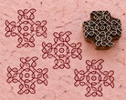 Hand carved wooden rangoli pattern printing block beside a dark red symmetrical rangoli impression on textured handmade paper.