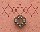 Hand carved wooden geometric tile printing block beside a repeating interlocking border pattern printed in burgundy on textured pink handmade paper.