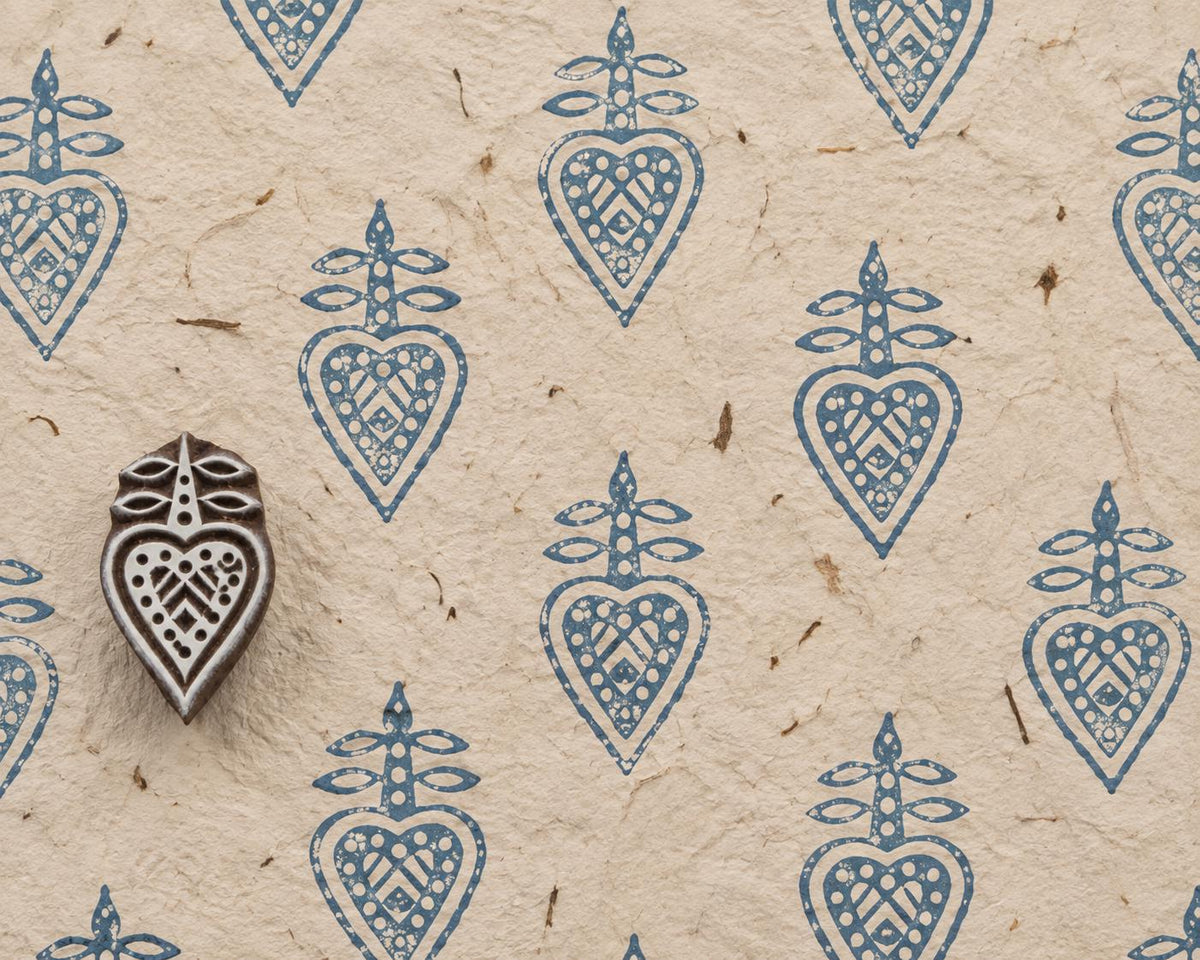 Hand carved Indian wooden printing block with an ornamental heart-shaped motif and geometric interior detail, shown with repeated blue impressions on handmade paper.