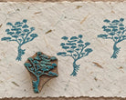Hand carved wooden Rooted Tree printing block with blue-green tree impressions on textured handmade paper.