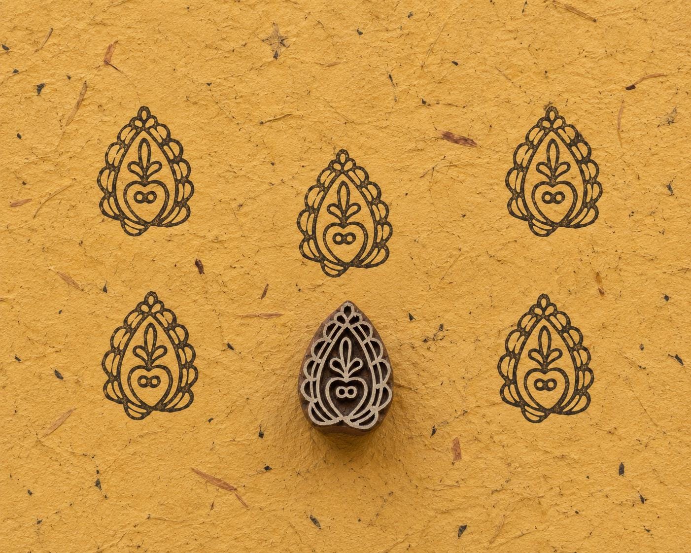 Hand carved wooden Pomegranate Paisley printing block with repeated impressions on textured handmade paper.