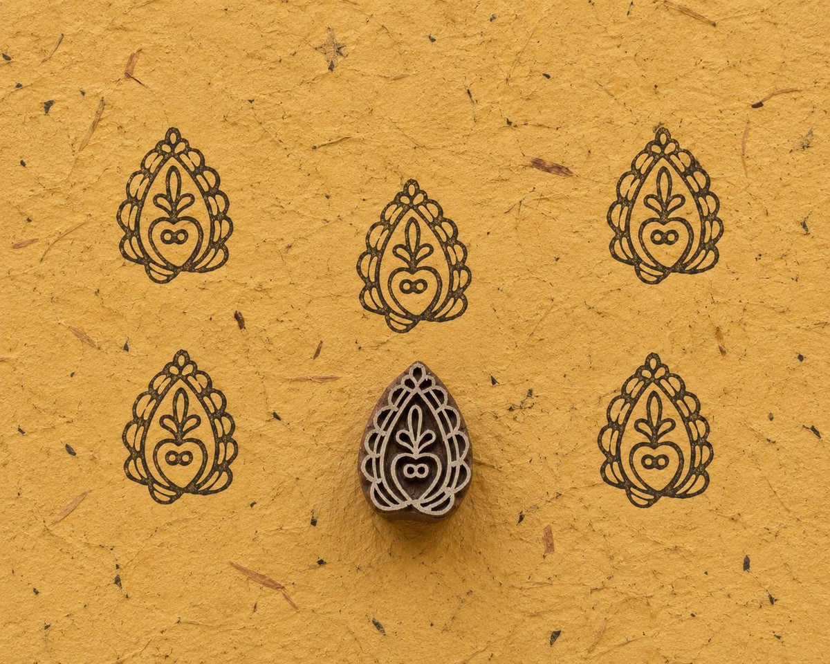 Hand carved wooden Pomegranate Paisley printing block with repeated impressions on textured handmade paper.