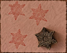 Hand carved wooden Floral Starburst printing block with repeated red impressions on textured pink handmade paper.