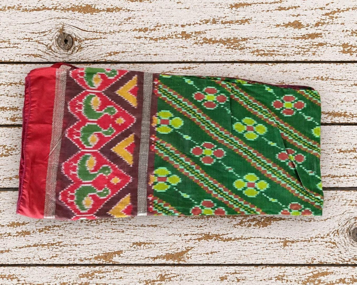 Vintage green Indian silk sari textile laid flat showing its red yellow and burgundy geometric floral pattern and decorative border