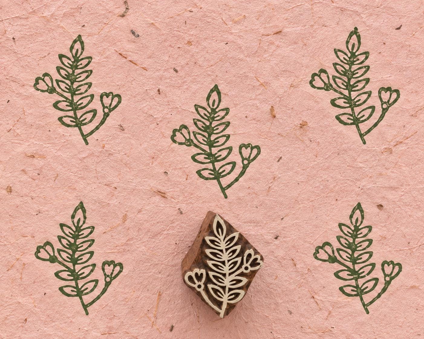 Heartbud Sprig 3cm hand carved wooden printing block with repeated green botanical impressions on pink handmade paper.