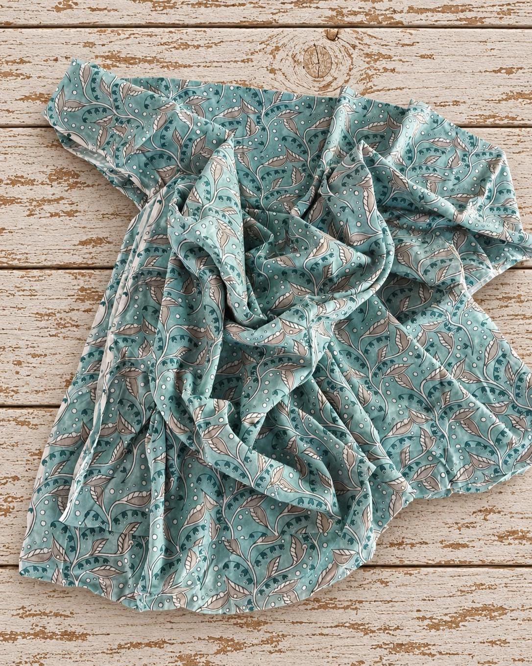 Soft mulmul cotton fabric showing the drape of the aqua blue Indian trailing leaf print