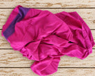Close-up of fuchsia silk fabric showing its fine texture and contrasting purple striped border