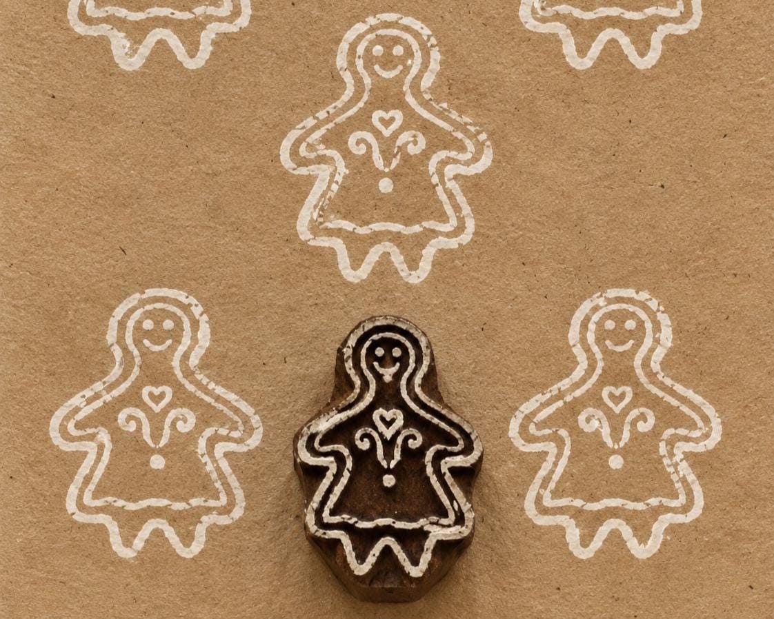 Gingerbread Girl hand carved wooden printing block with repeated white impressions on kraft paper.