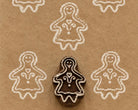 Gingerbread Girl hand carved wooden printing block with repeated white impressions on kraft paper.