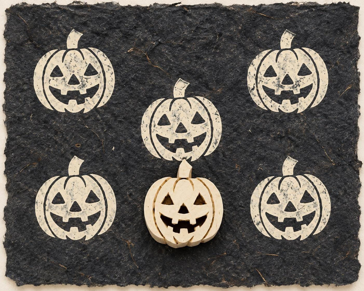 Hand carved Jack-O-Lantern wooden printing block with repeated pumpkin impressions on black handmade paper.