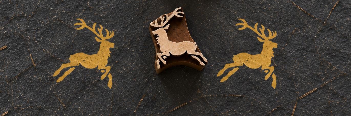 Wooden Christmas printing block featuring a leaping reindeer with antlers, shown with repeated golden prints on dark handmade paper.