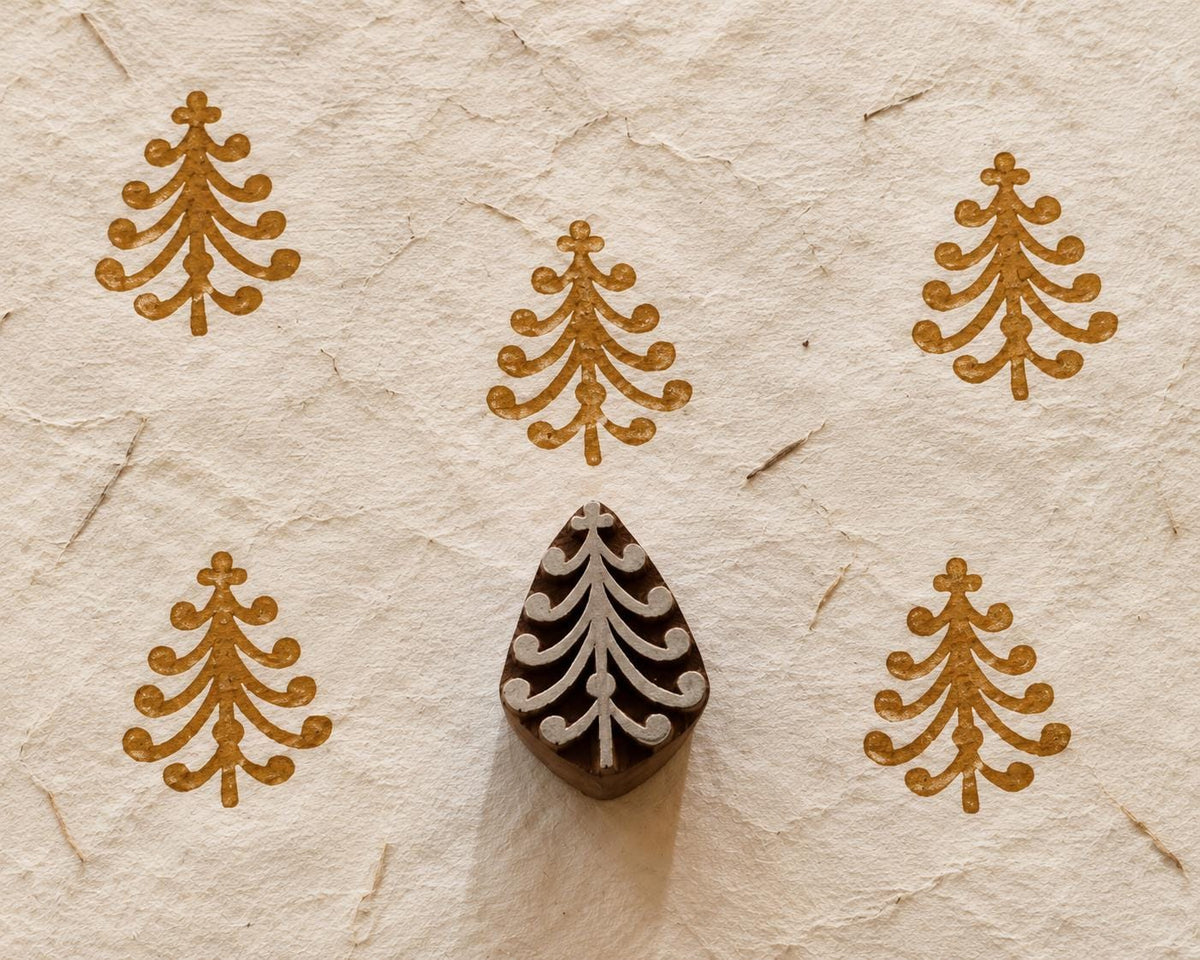 Wooden Christmas printing block featuring a whimsical Christmas tree with curled branches and rounded ornaments, shown with brown prints.