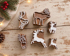 Five hand carved wooden printing blocks featuring different Christmas reindeer and stag designs arranged on a distressed white wooden table.