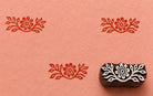Hand-carved wooden floral border printing block shown beside repeated folk floral prints on handmade paper