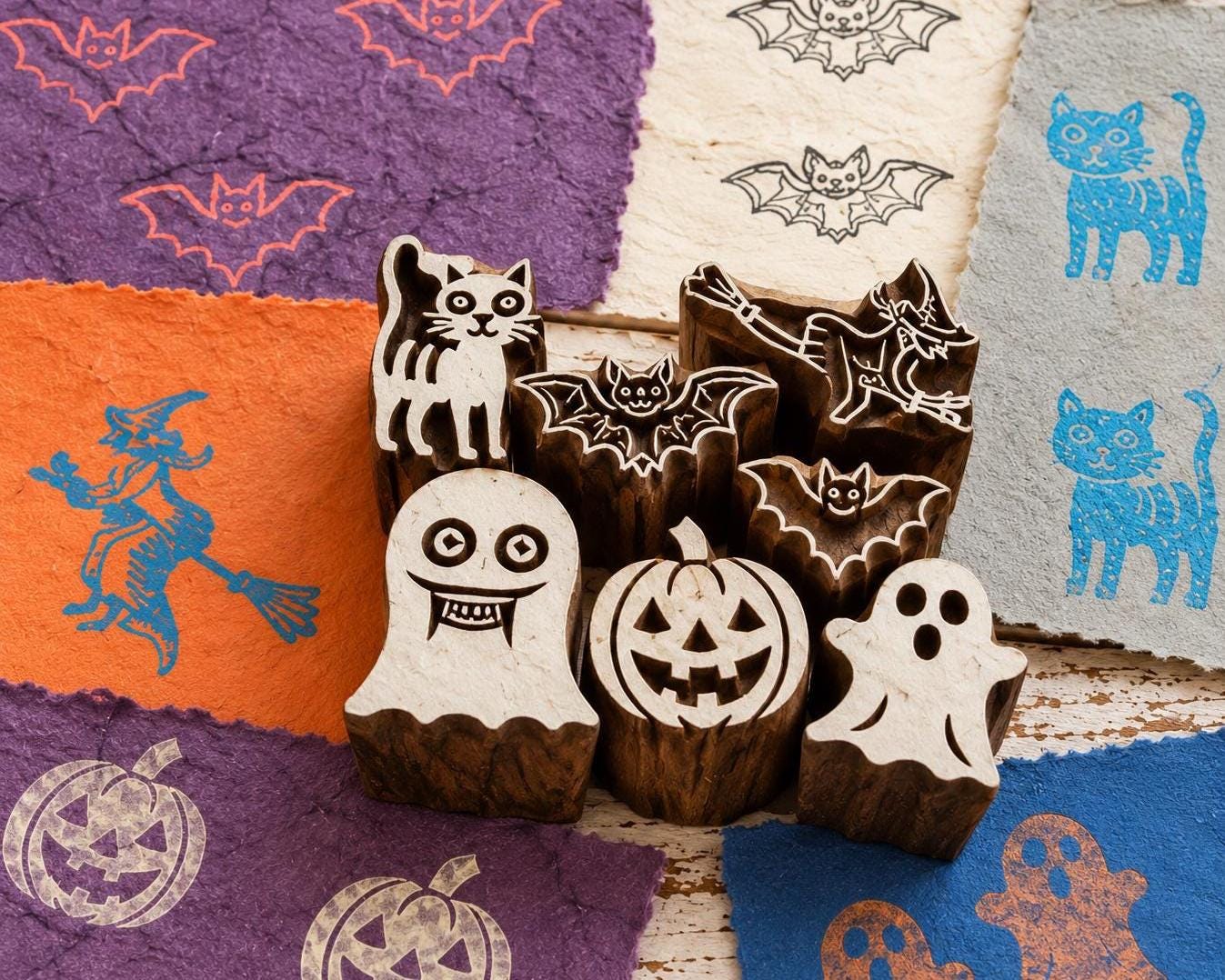Seven hand carved wooden Halloween stamps featuring a cat, bats, ghost, pumpkin and witch, shown with printed examples on handmade paper.
