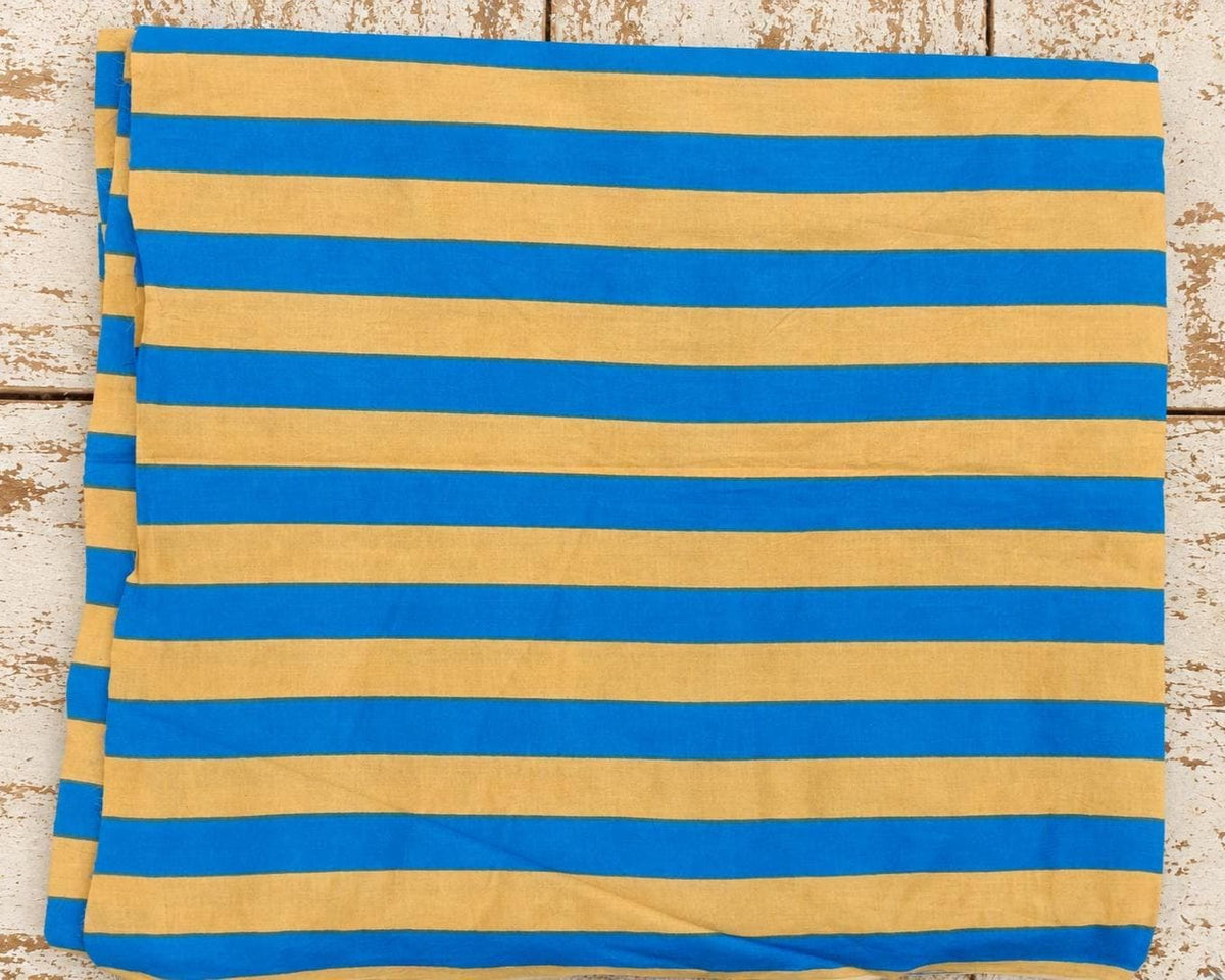 Close view of blue and beige 1.5 inch stripes on lightweight hand screen printed cotton fabric on flatlay table