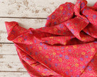 Vintage coral-red sari silk fabric with small blue and yellow flowers, folded on a rustic white wooden surface.