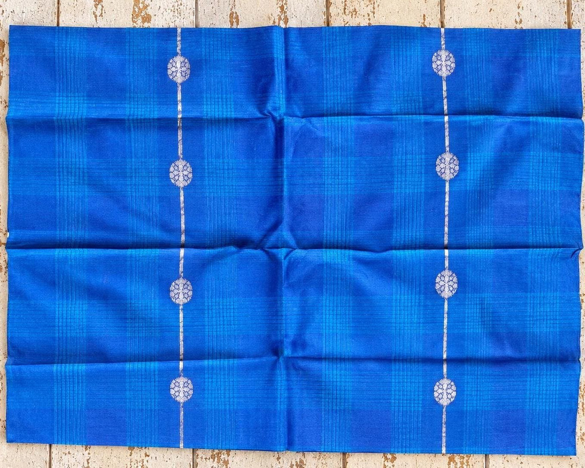 Square blue textile showing turquoise checked lines and repeating silver motifs.
