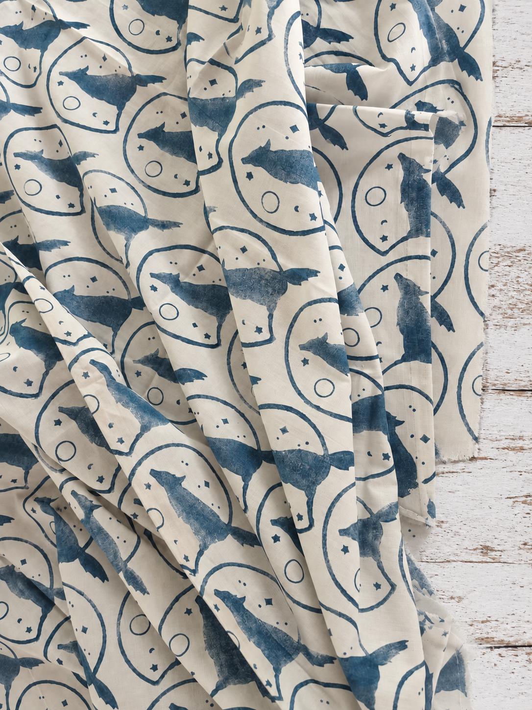 Soft cotton fabric with repeating indigo howling wolf and moon print shown in a drape