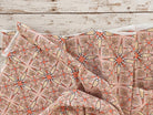Soft peach cotton fabric with repeating floral starburst pattern shown in a drape